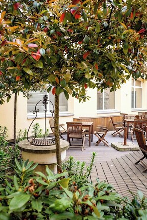 An outdoor patio with wooden furniture and a decorative metal planter. - Hotel Konigshof Am Funkturm (Hannover)