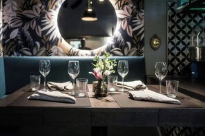 A dining table set with wine glasses and a vase of flowers, with a patterned wall and a sofa in the background. - Hotel Konigshof Am Funkturm (Hannover)