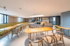A modern dining area with wooden tables and chairs, a kitchen in the background, and large windows providing natural light. - JI Hotel Shenzhen Convention Center (Shenzhen)