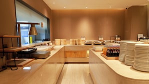 Un hall d’hôtel moderne avec un comptoir d’accueil central, une grande fenêtre et un présentoir proposant des aliments et des boissons.