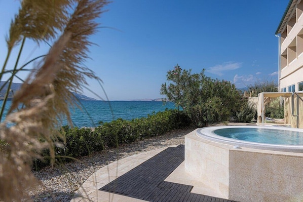 A pool area with a view of the sea, surrounded by greenery and a building with a modern design.