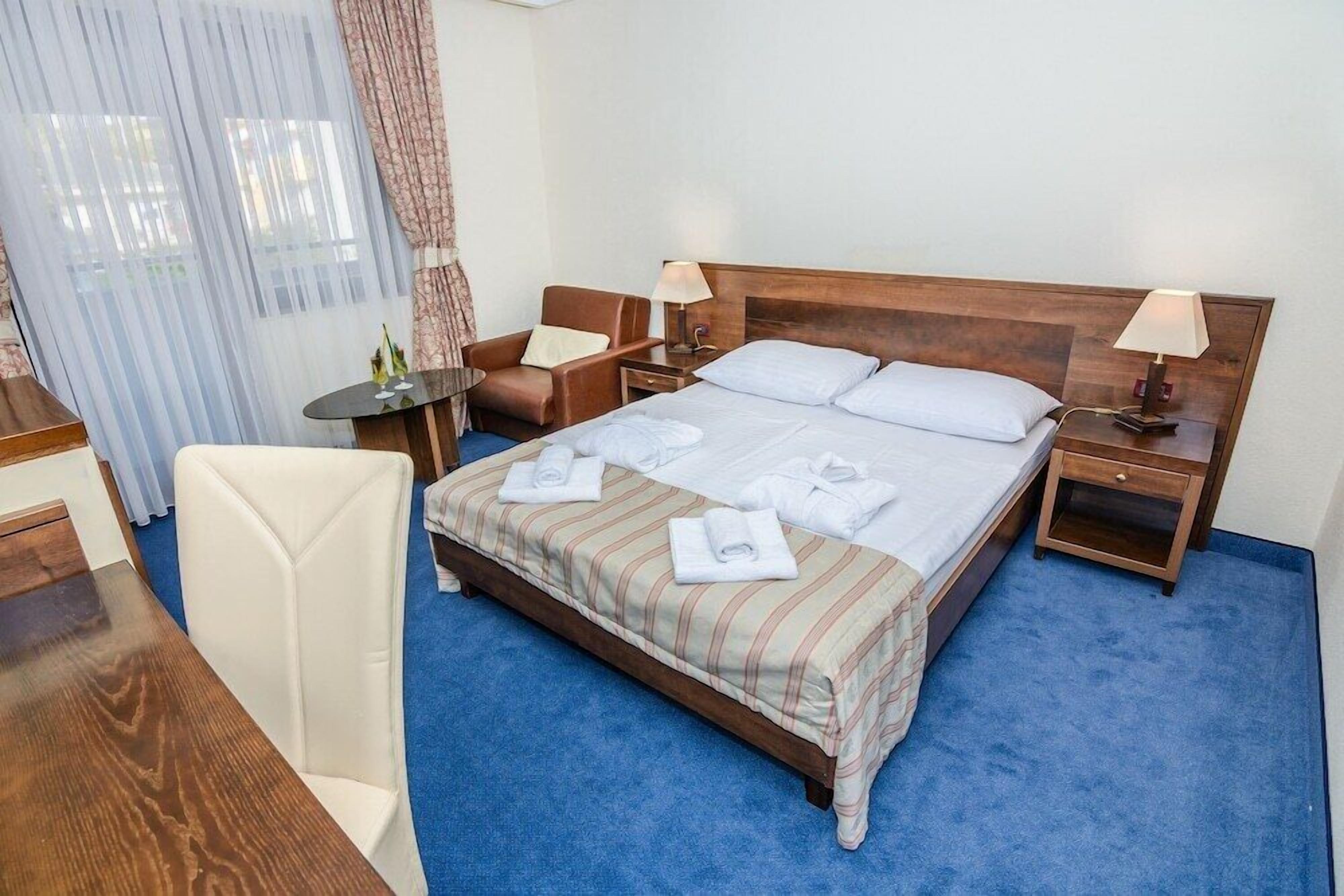 A hotel room with a large bed, two bedside tables, a chair, a desk, and a window with curtains.