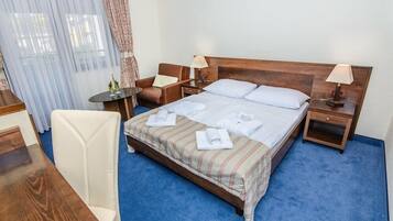A hotel room with a large bed, two bedside tables, a chair, a desk, and a window with curtains.