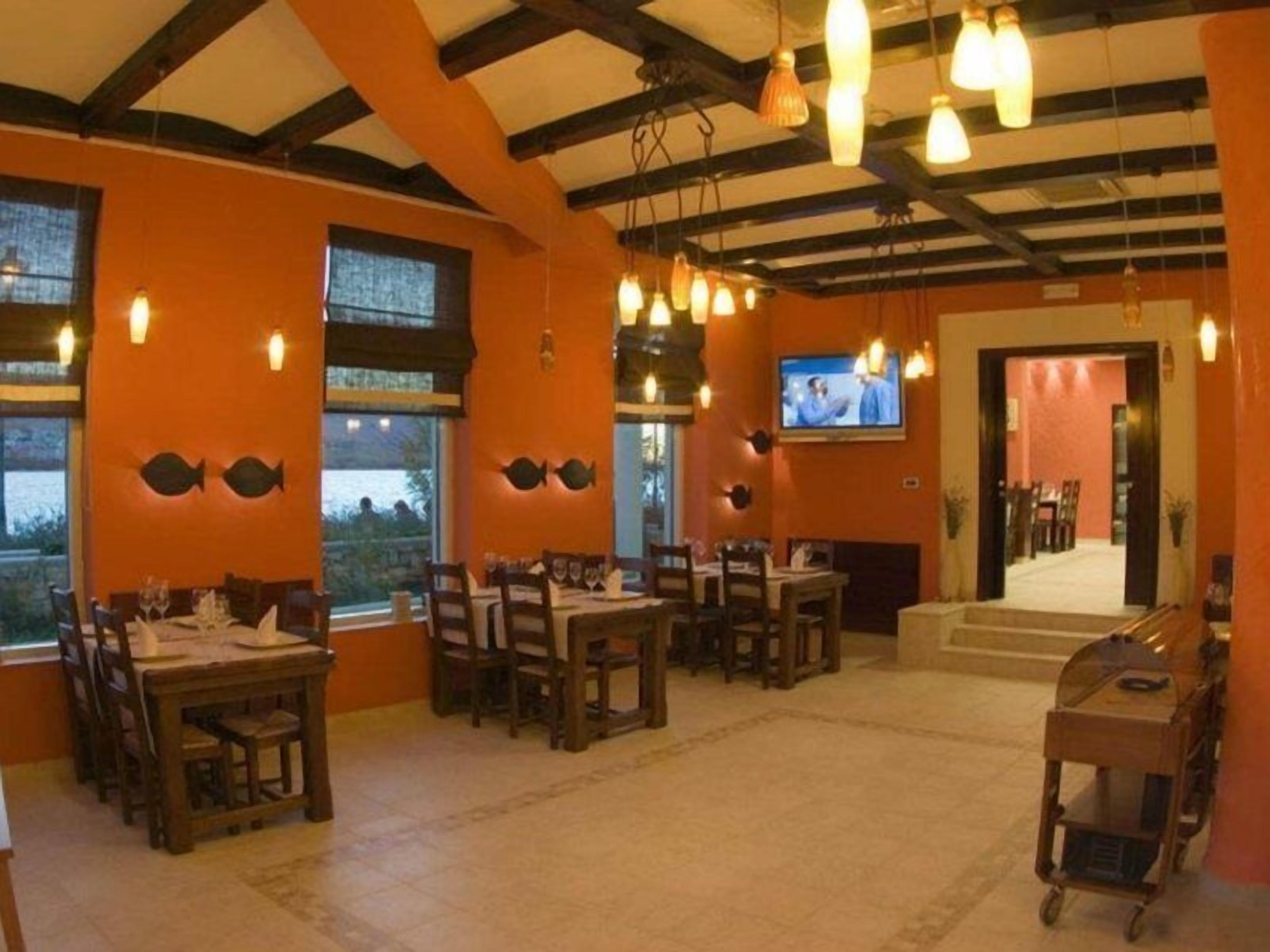 Un restaurante con mesas y sillas de madera, un televisor en la pared y vistas al exterior a través de amplias ventanas.