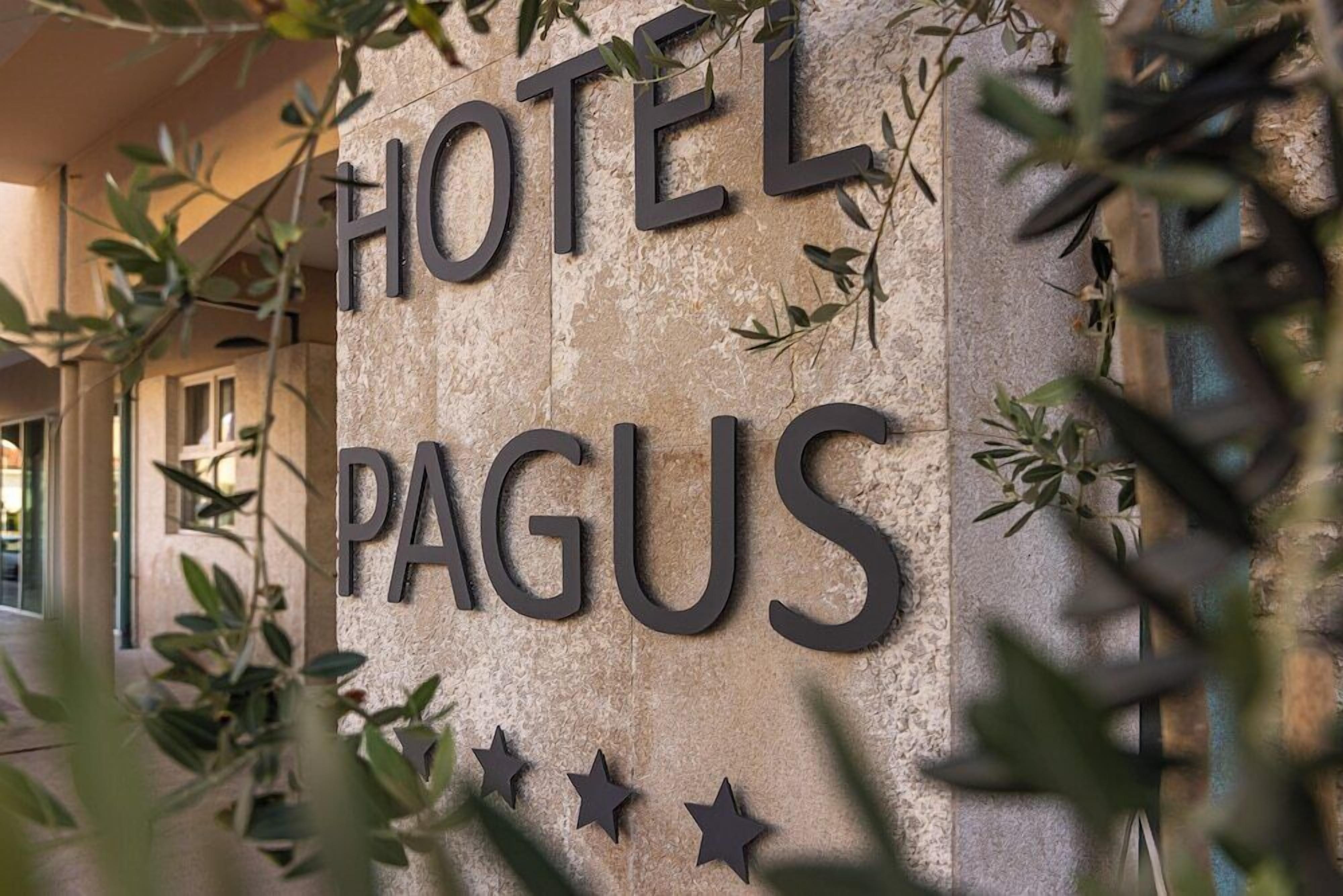 Un mur de pierre sur lequel on peut lire les mots « HÔTEL PAGUS » et trois étoiles.