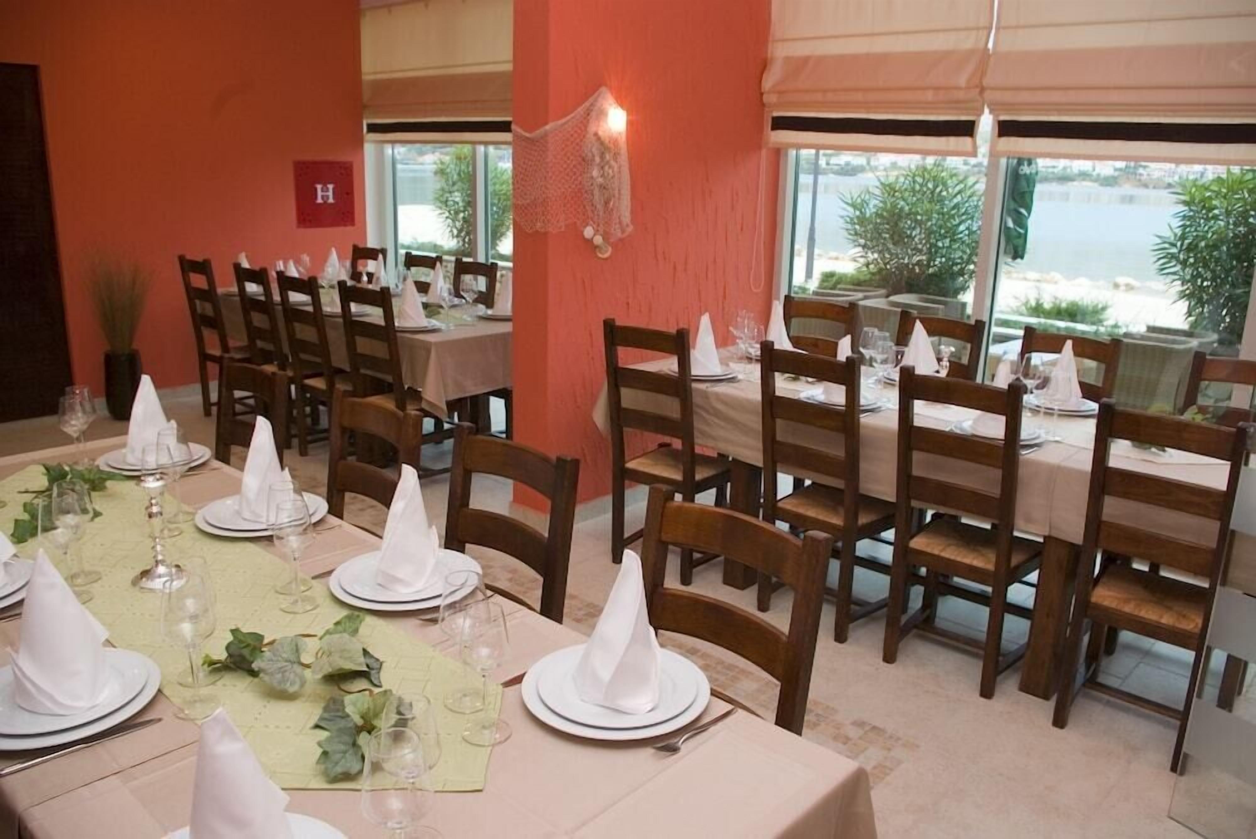 A dining area with tables set for a meal, chairs, and a view of the sea.