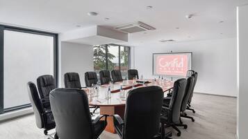 A conference room with a large table, black chairs, and a projector screen displaying 'Grifid Hotel'.