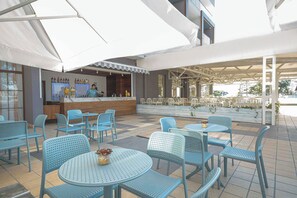 An outdoor seating area with blue chairs and tables, a bar with a counter, and umbrellas providing shade. - Sentido Marea (Varna)