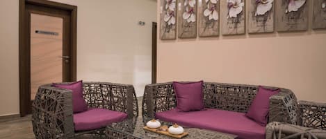 A room with wicker furniture, a glass table with two white teapots, and a wall with floral artwork.