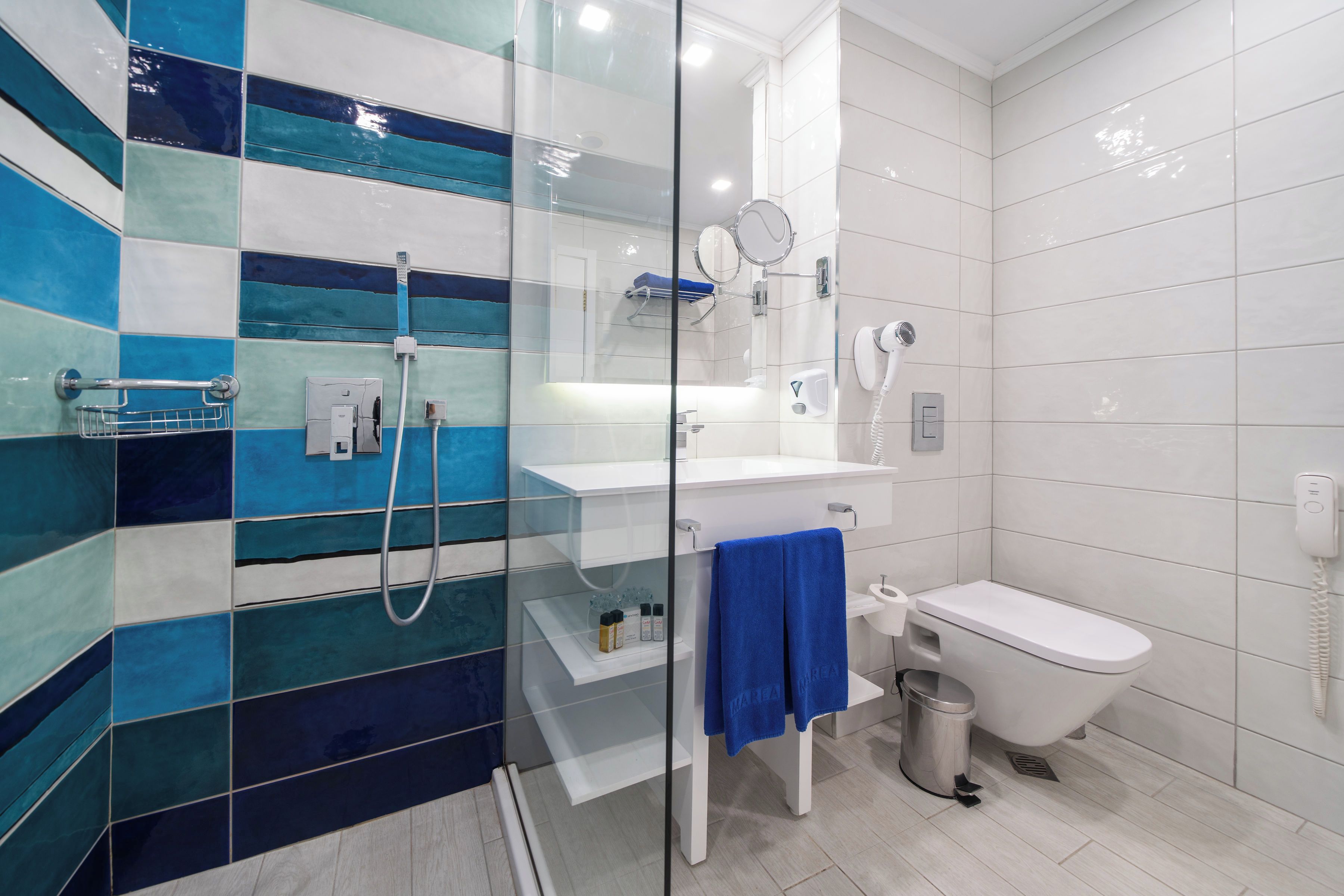 A bathroom with a glass shower enclosure, a white sink, a toilet, and a blue towel hanging on the wall.