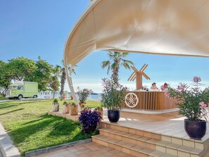 A covered outdoor seating area with a windmill, potted plants, and a green truck in the background. - Sentido Marea (Varna)