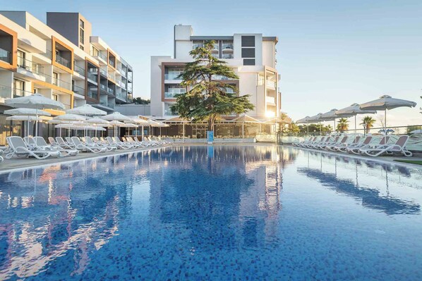 A swimming pool with lounge chairs and umbrellas, surrounded by modern buildings. - Sentido Marea (Varna)