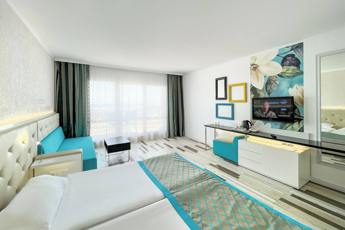 Une chambre d’hôtel avec un lit, un bureau, une télévision et une grande fenêtre avec des rideaux.