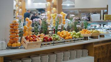 A buffet with various fruits and vegetables, including oranges, apples, and bananas, arranged on a counter with plates and bowls.