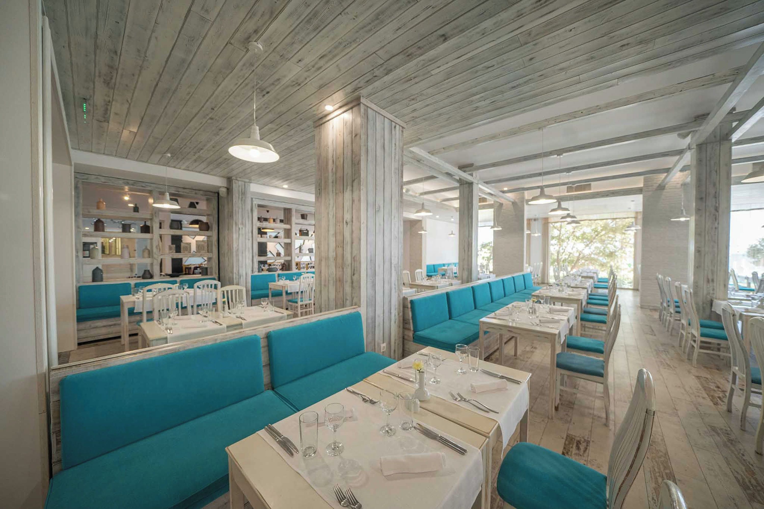 A restaurant with wooden ceilings, teal seating, and white tables.