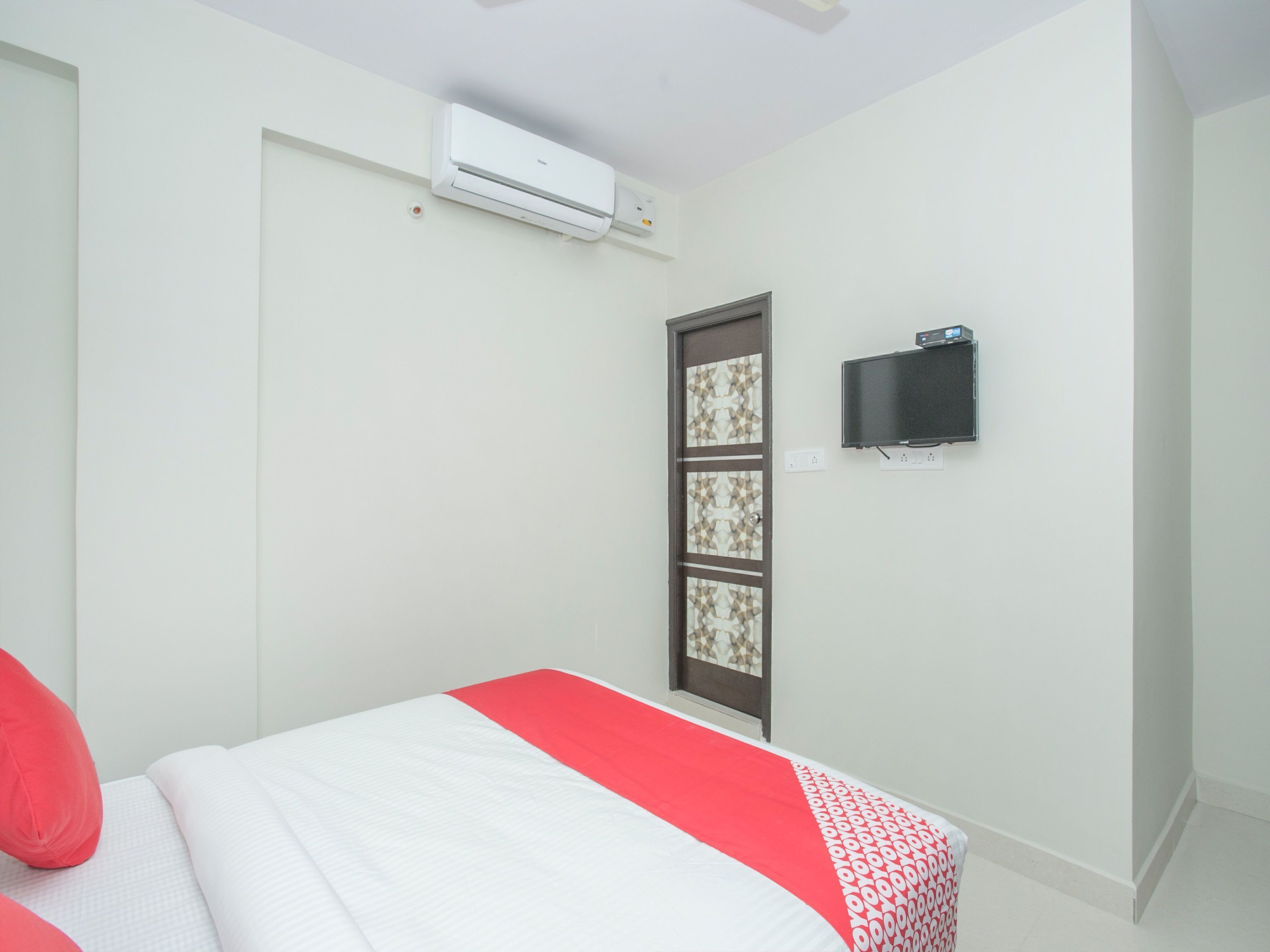 A hotel room with a bed, a television mounted on the wall, and an air conditioning unit above the bed.