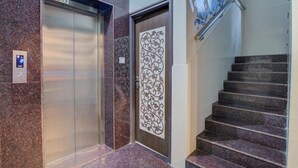 Un ascensor, una puerta decorativa y una escalera con barandilla.