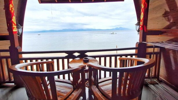 Terraza de madera con una mesa y sillas, con vista a un cuerpo de agua tranquilo y montañas a lo lejos.