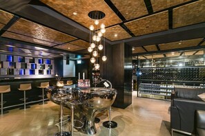 Eine moderne Bar mit einer markanten Metallskulptur, einer Auswahl an Flaschen in Regalen und einer Bar, ausgestattet mit Hockern.