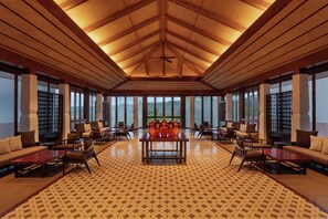 A spacious lobby with a high ceiling, a central table, seating arrangements, and large windows.