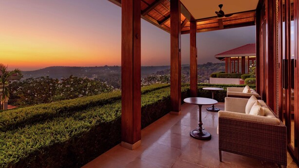 A covered outdoor seating area with a view of a sunset and hills. - Hilton Goa Resort (Candolim)