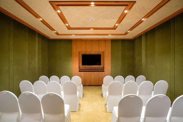 A conference room with a large screen, rows of white chairs, and a wooden panel wall.