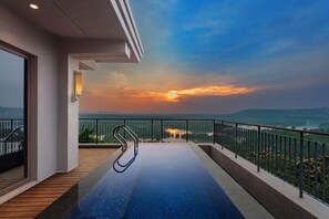 A rooftop pool with a view of a sunset over a mountainous landscape.
