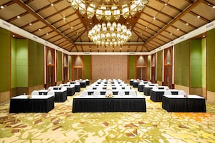 Un salón de conferencias con varias mesas, una araña y una alfombra estampada.
