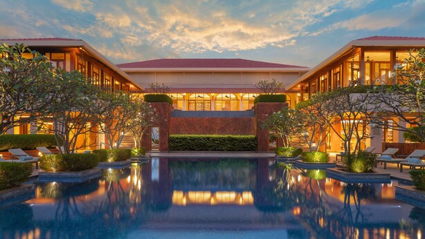 Un hotel con una piscina amplia, zonas de descanso y una entrada bien iluminada.