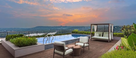 A rooftop pool area with a view of the city, a wooden deck, and outdoor furniture.