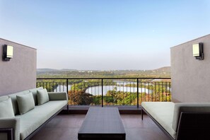 A balcony with a sofa and a small table, offering a view of a lake and surrounding greenery.