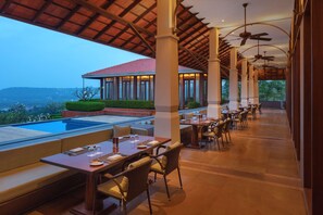 An outdoor dining area with tables and chairs, a pool, and a view of the landscape. - Hilton Goa Resort (Candolim)