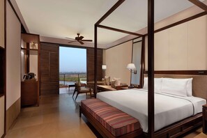 A four-poster bed with a view to the outdoors, a ceiling fan, a bedside table with a lamp, and a bench at the foot of the bed. - Hilton Goa Resort (Candolim)