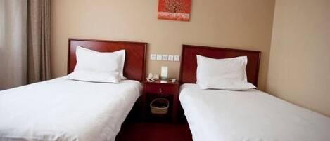 A hotel room with two single beds, a wooden headboard, a nightstand with a phone and a lamp, and a red artwork on the wall.