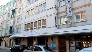 Il s’agit d’un hôtel à plusieurs étages, reconnaissable à son enseigne bien visible où l’on peut lire « HÔTEL CABAZA ». Plusieurs voitures sont garées devant, et le bâtiment présente un style architectural classique, avec de grandes fenêtres et un toit plat.