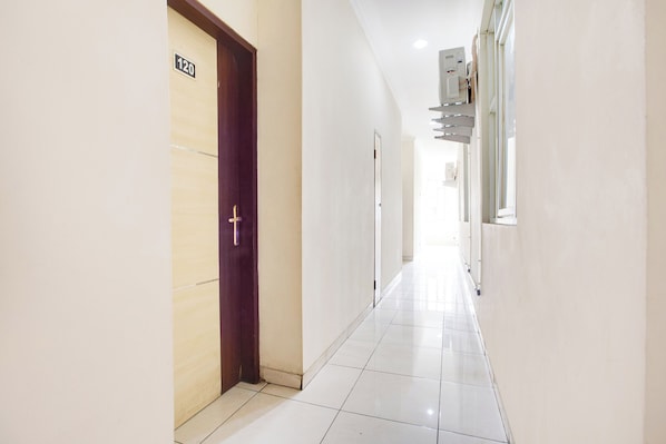A corridor with a wooden door marked "120", a white tiled floor, and a ceiling-mounted air conditioning unit. - Reddoorz @ Hotel Arimbi Dewi Sartika Baru (Bandung)