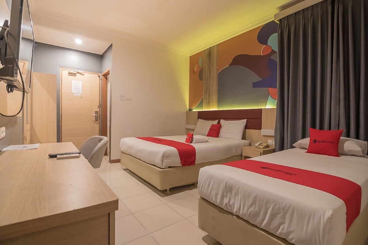 A hotel room with two beds, a desk, a chair, and a door.