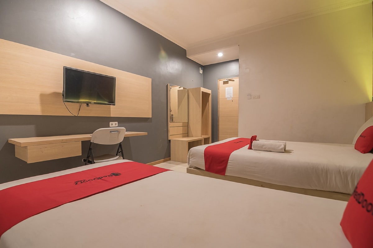 A hotel room with two beds, a desk, a chair, a TV, and a mirror.