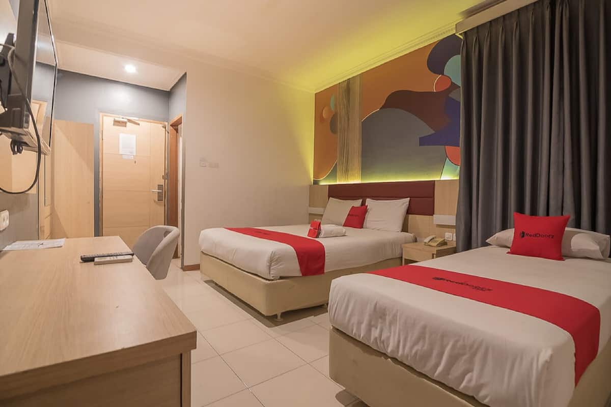 A hotel room with two beds, a desk, a chair, and a door.