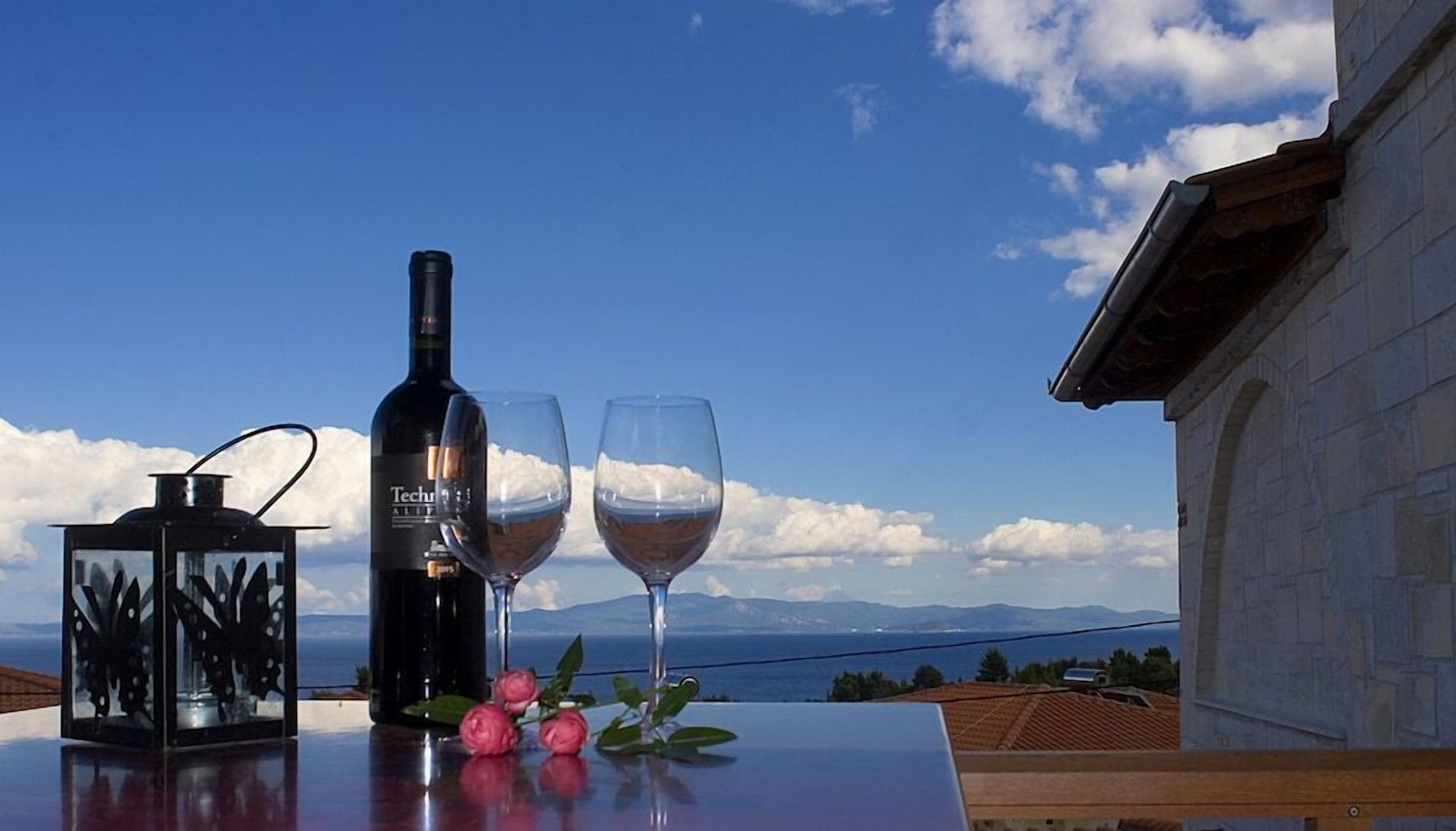 A bottle of wine and two glasses on a table with a view of the sea and mountains.