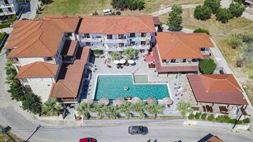 An aerial view of a resort with multiple buildings, a central swimming pool, and surrounding greenery.