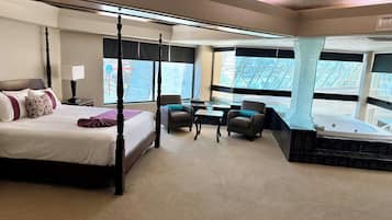 Una cama con dosel y cabecera de mármol, un área de estar con dos sillones, una mesita y una bañera.