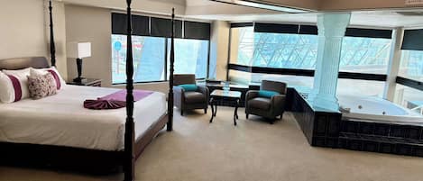 A four-poster bed with a marble headboard, a sitting area with two chairs, a small table, and a bathtub.