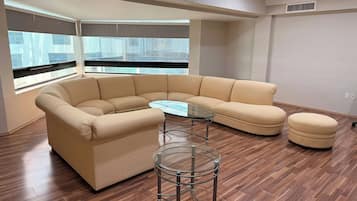 Una sala de estar moderna con un sofá seccional color beige, una mesa de centro de vidrio y un reposapiés redondo.