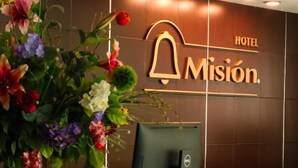 Eine Rezeption mit einem Computer und einer großen Blumenkomposition. An der Wand ist der Schriftzug "HOTEL Misión" zu sehen.