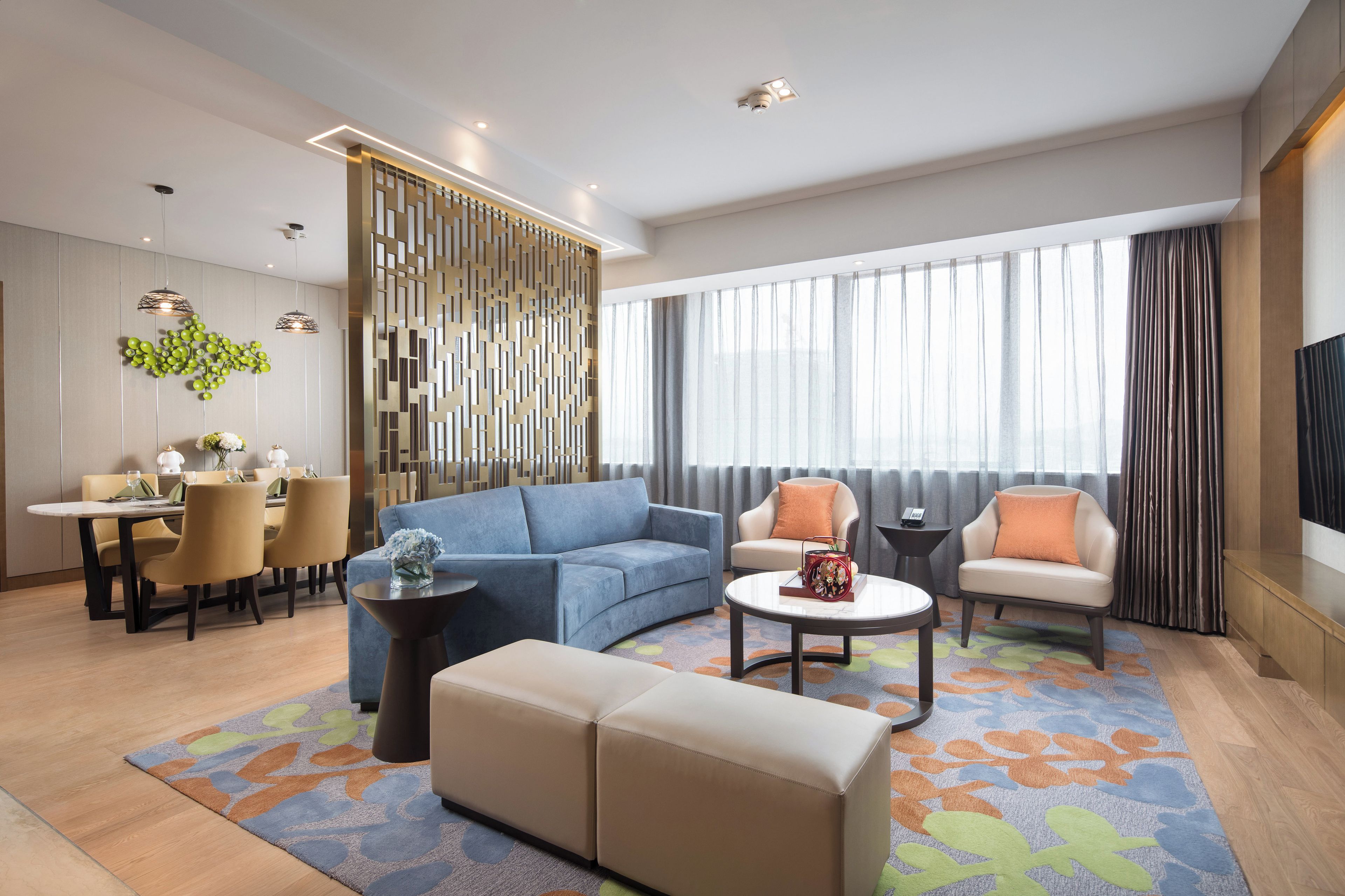 A modern living room with a sofa, ottoman, coffee table, and a dining area with chairs and a table.