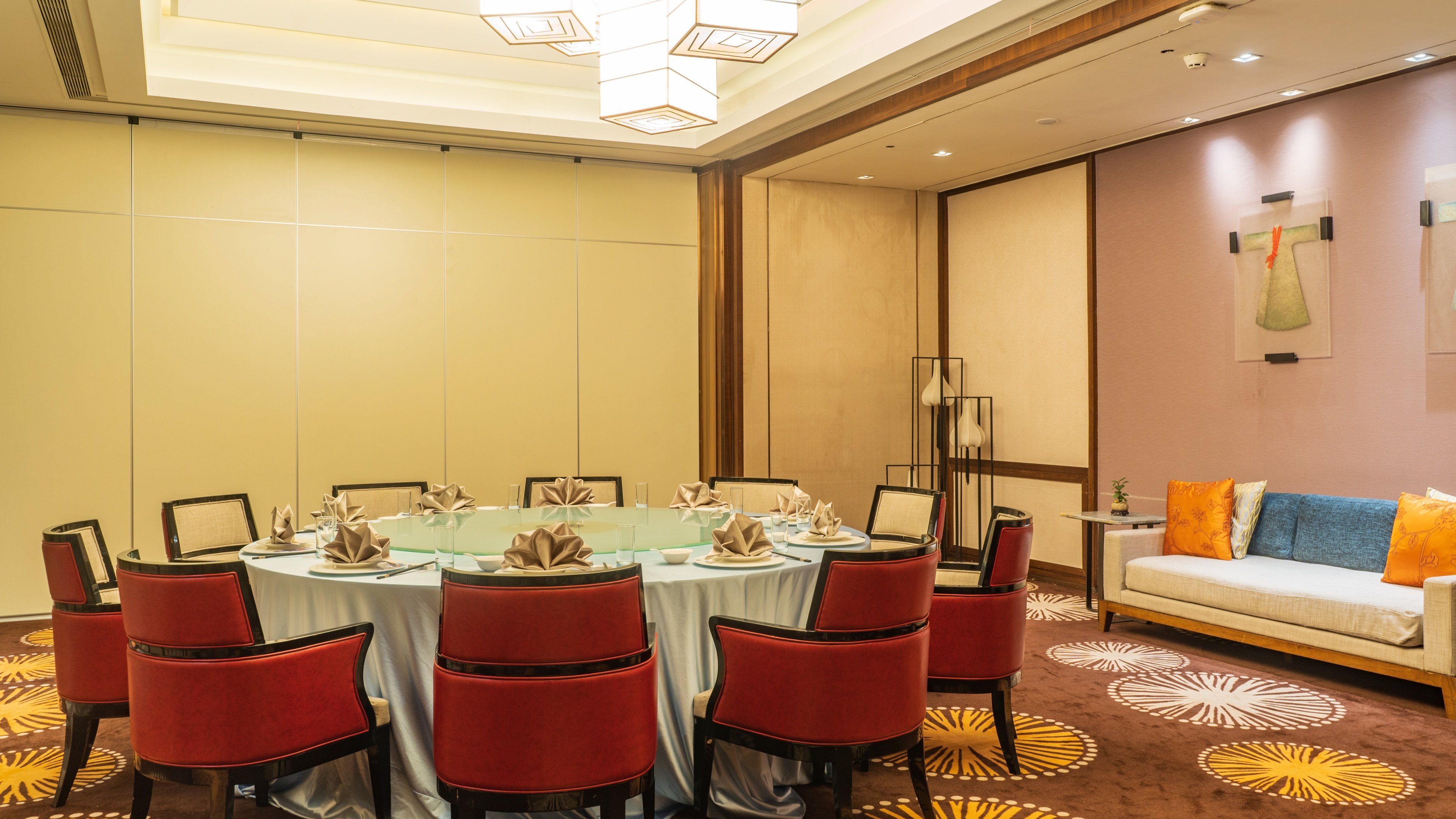 A conference room with a round table, red chairs, and a sofa with cushions.