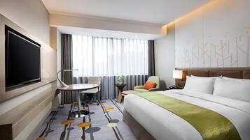 A hotel room with a large bed, a desk, a chair, a TV, and a window with curtains.