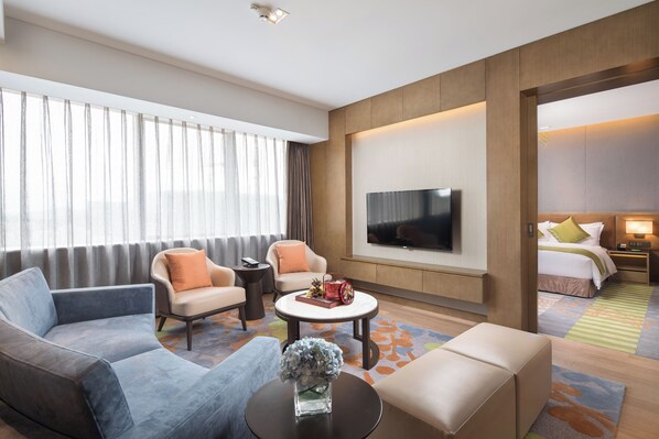 A hotel room with a sofa, armchair, coffee table, TV, and a bed with a nightstand. - Holiday Inn Shaoguan Downtown Hotel (Shaoguan)