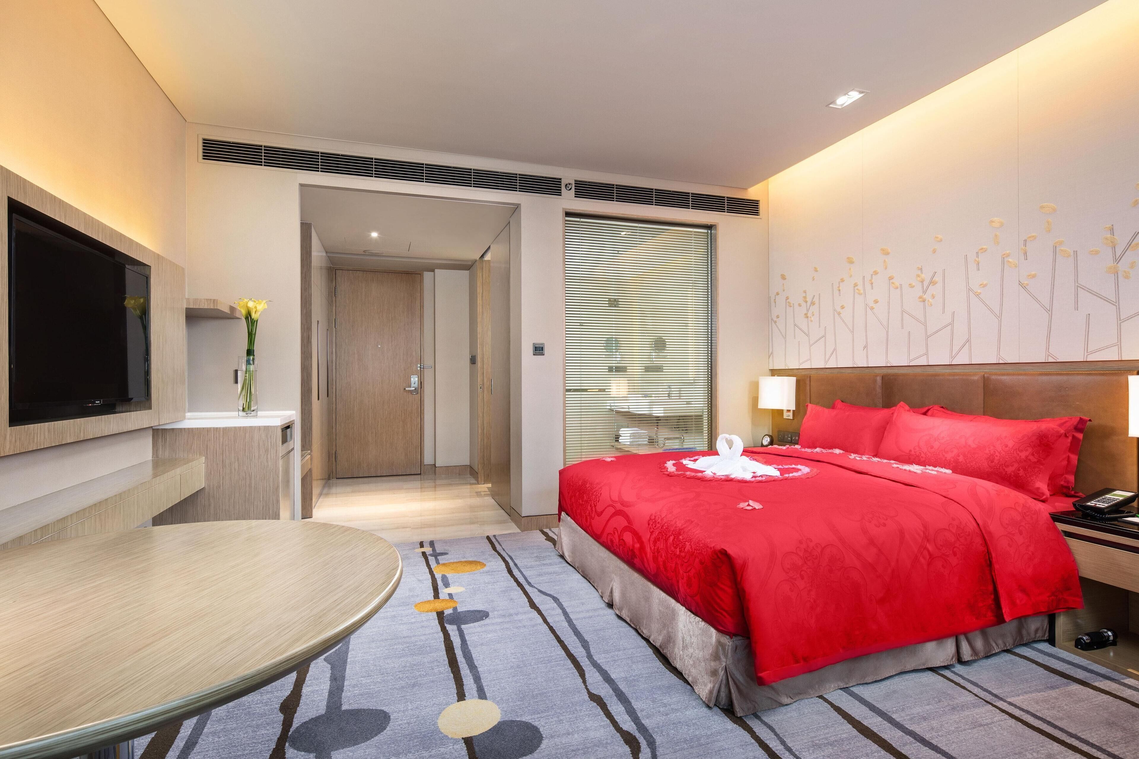 A modern hotel room with a large bed, a flat-screen TV, a dining table, and a bathroom visible through an open door.